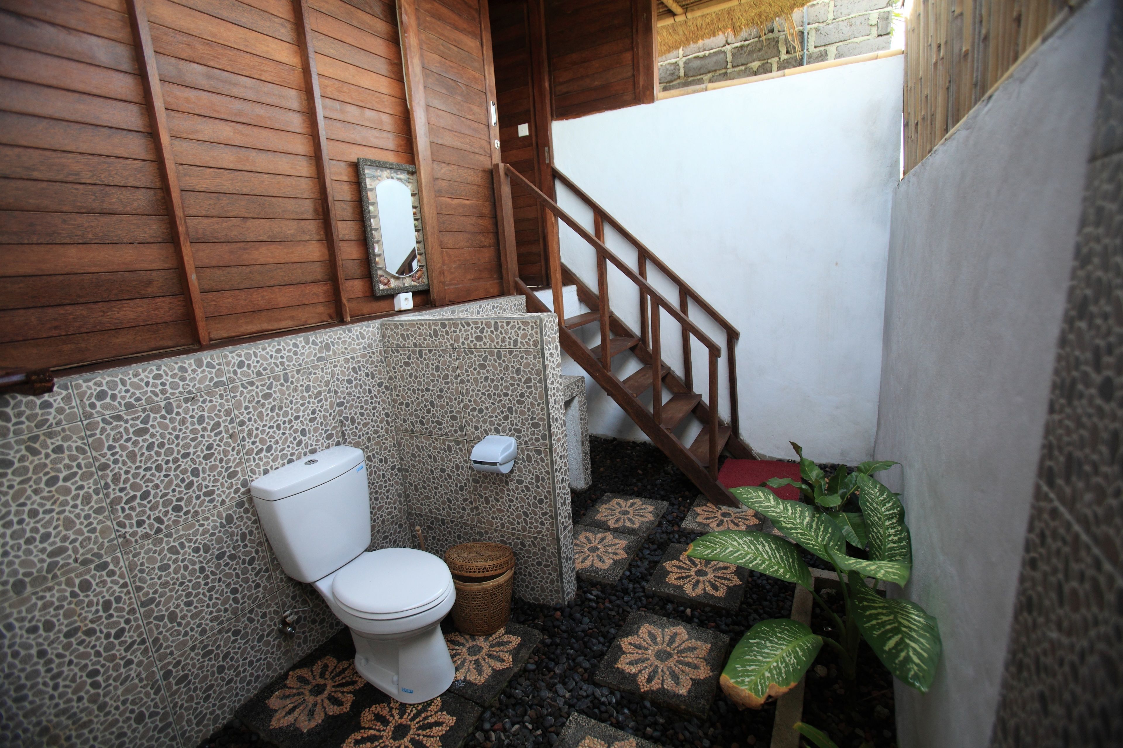 Ein Badezimmer mit Toilette, einer Holztreppe, einem Spiegel und einer Topfpflanze.