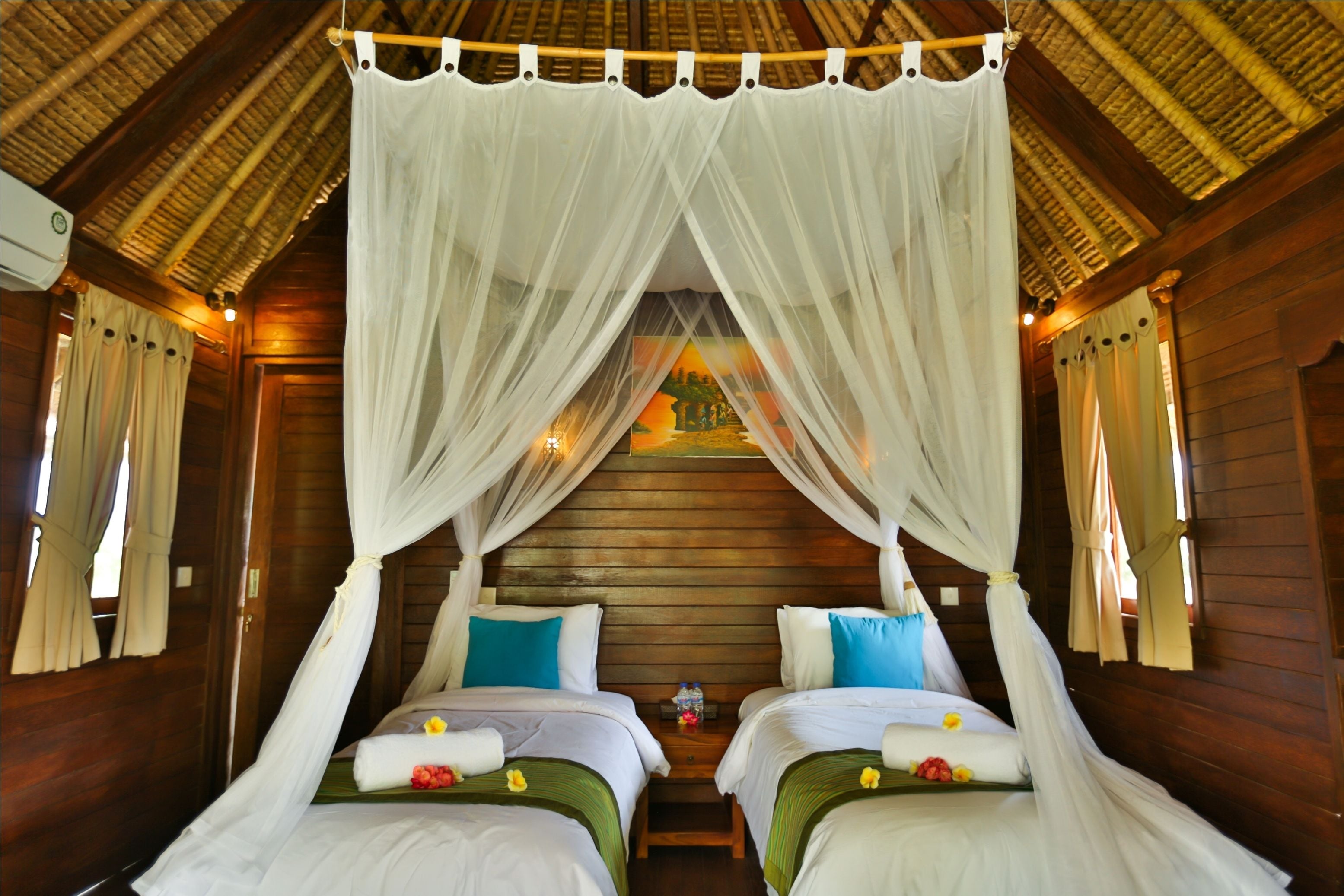 Habitación con dos camas, cada una con ropa blanca y almohadas azules, bajo un dosel.