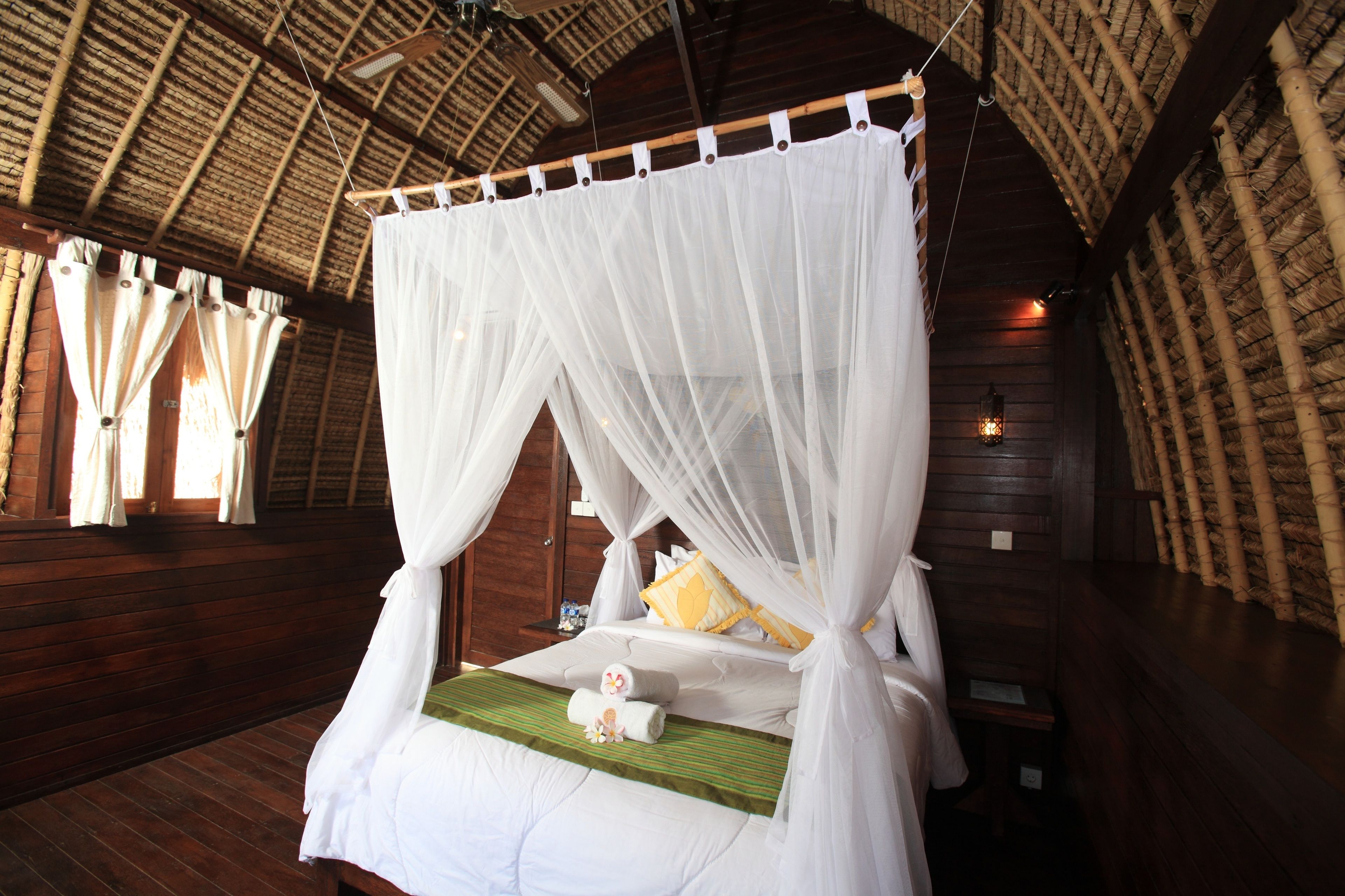 A bed with a canopy in a wooden room with a thatched roof.