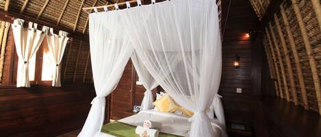 A bed with a canopy in a wooden room with a thatched roof.