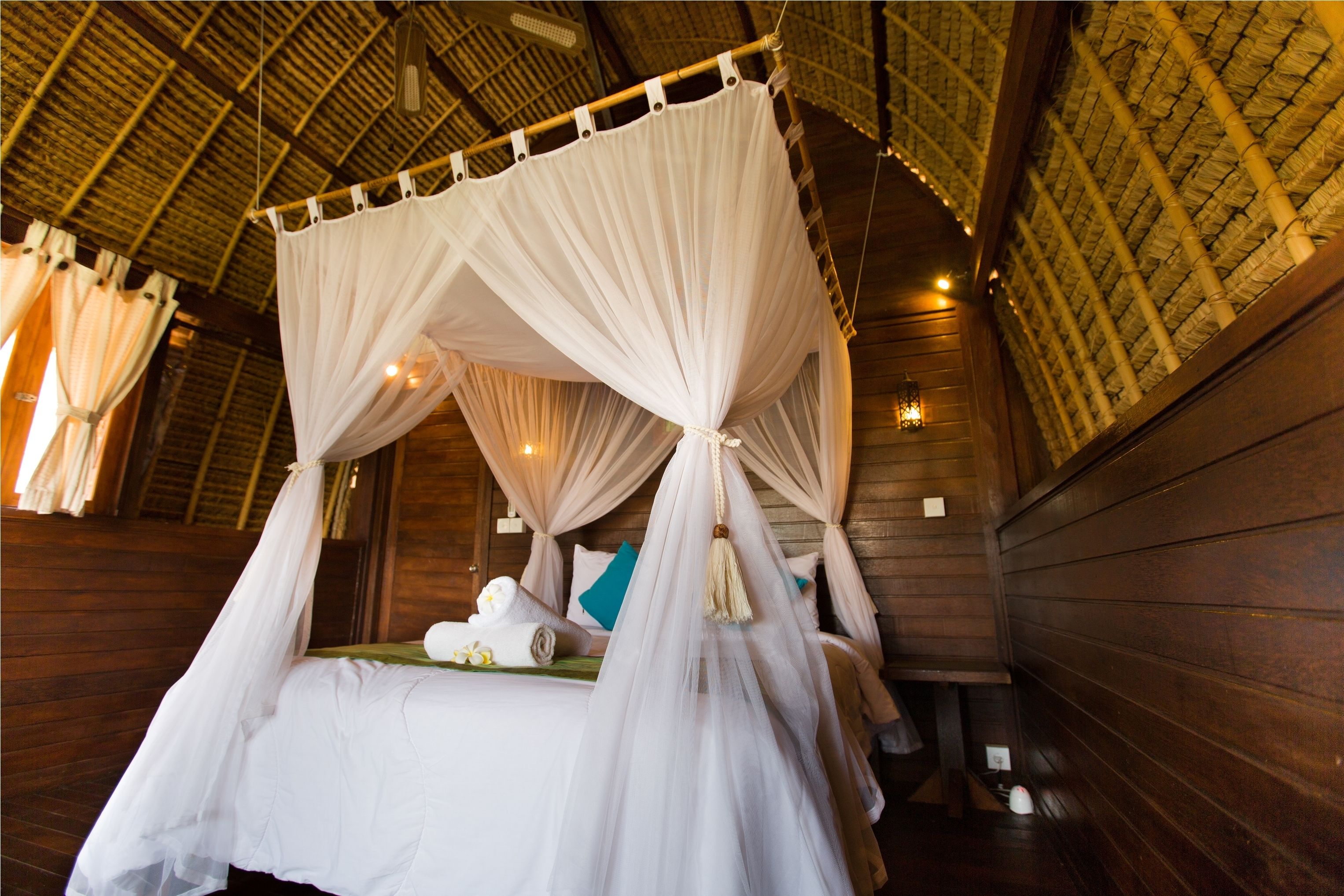 A four-poster canopy bed in a wooden room with a thatched roof.