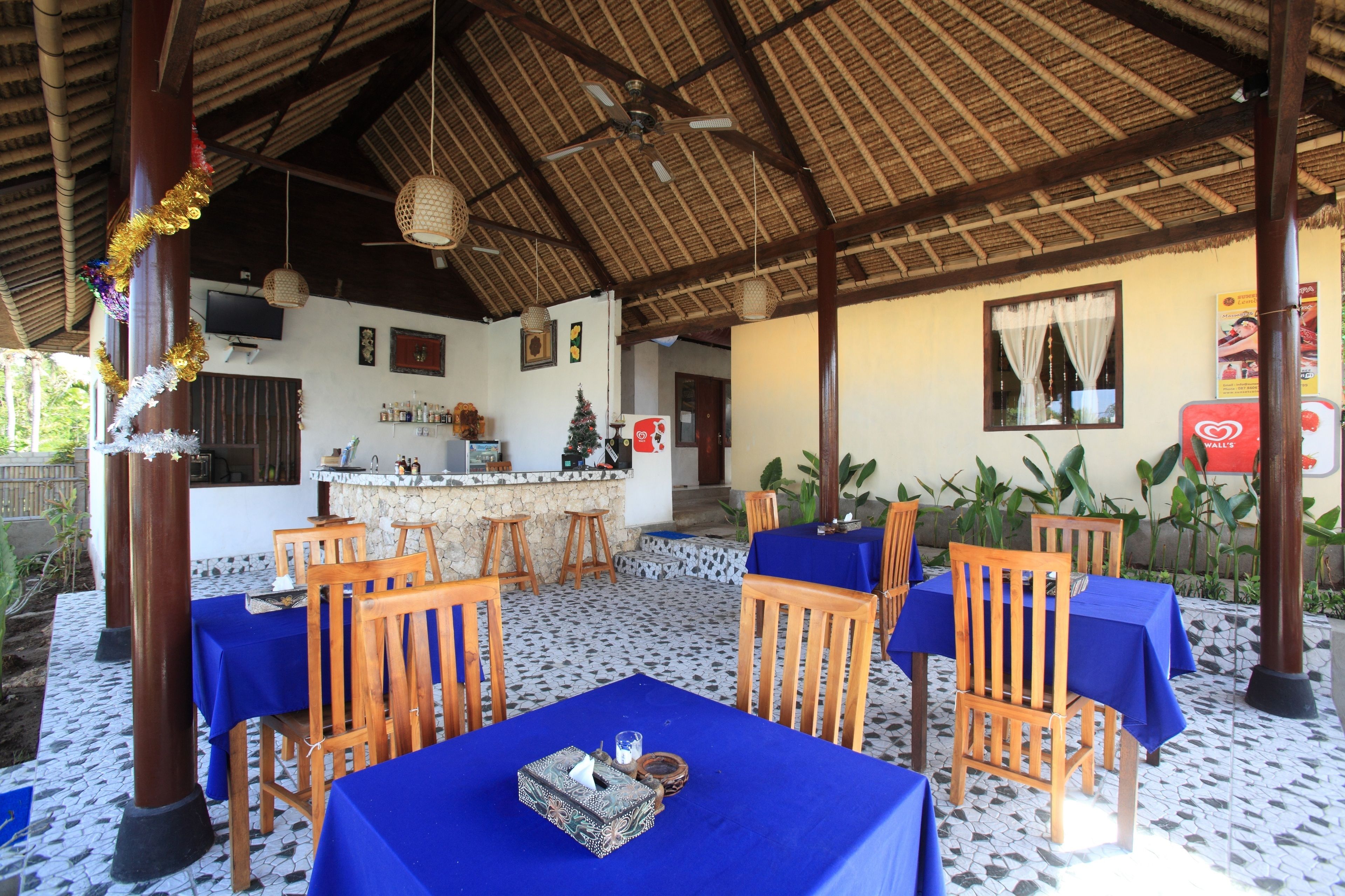 An outdoor dining area with tables and chairs, a bar, and a thatched roof.