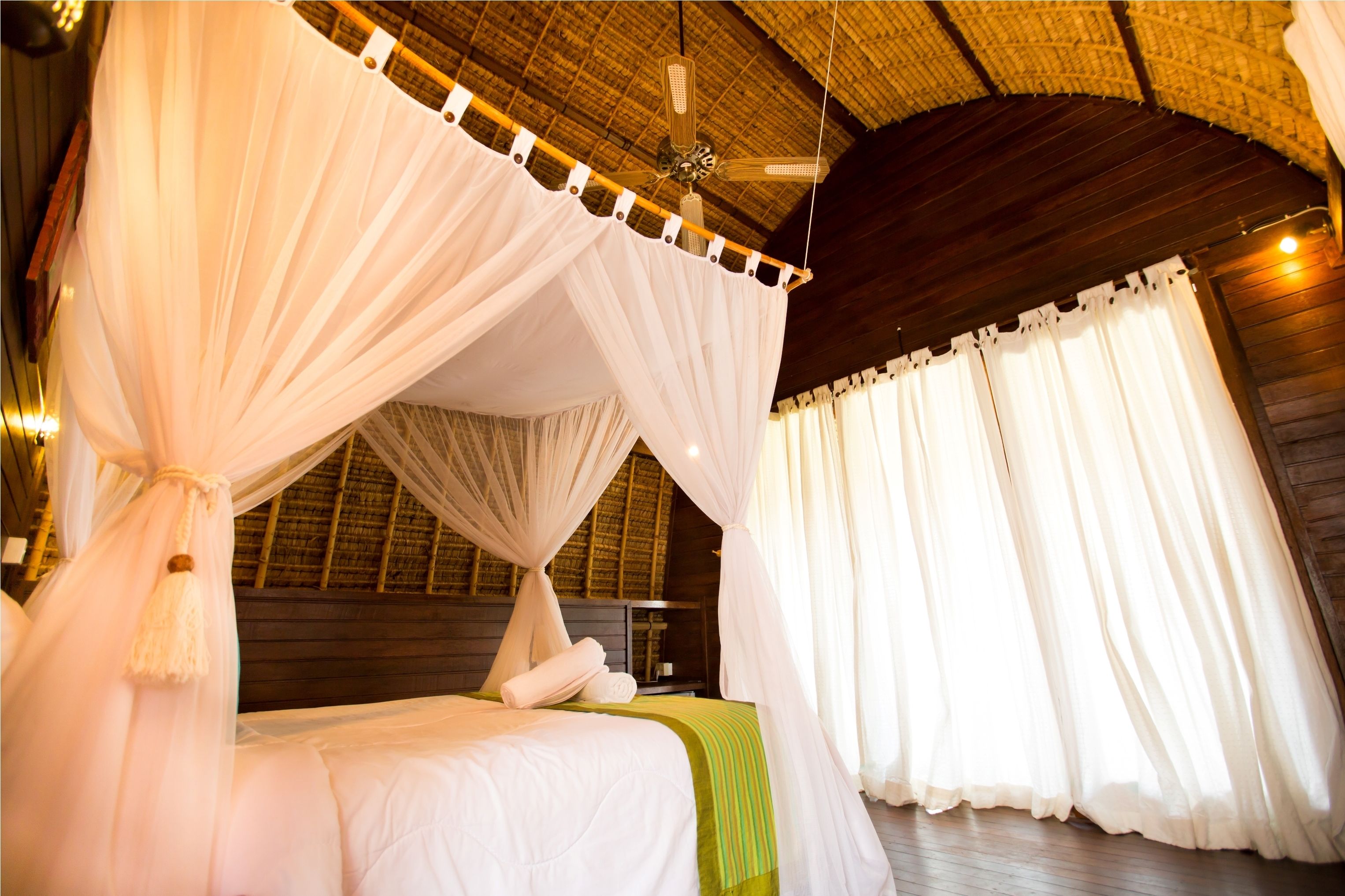 Una habitación con cama, cortinas blancas y ventilador de techo.