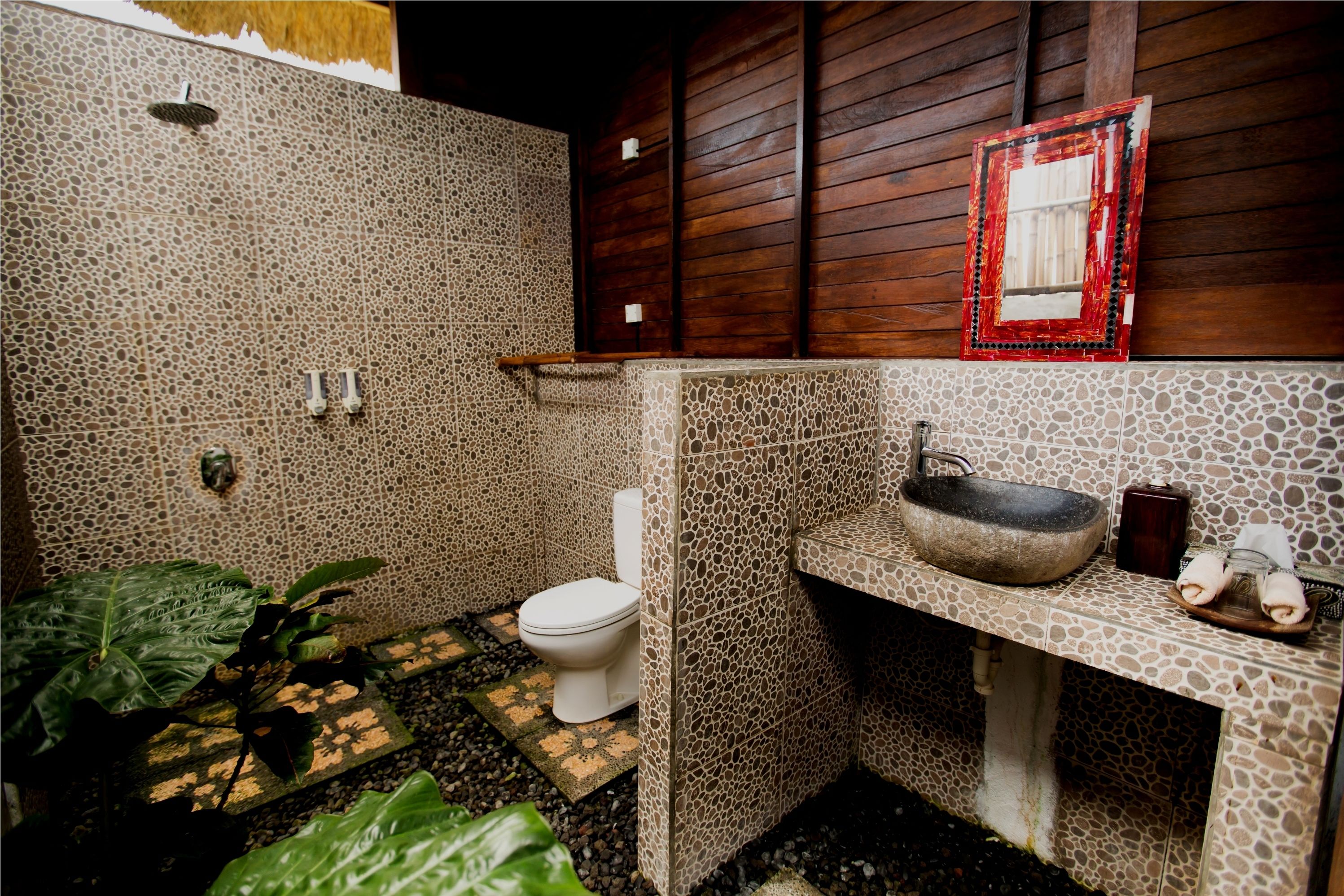Een badkamer met een stenen mozaïek vloer, een wit toilet, een stenen wastafel en een houten wand.