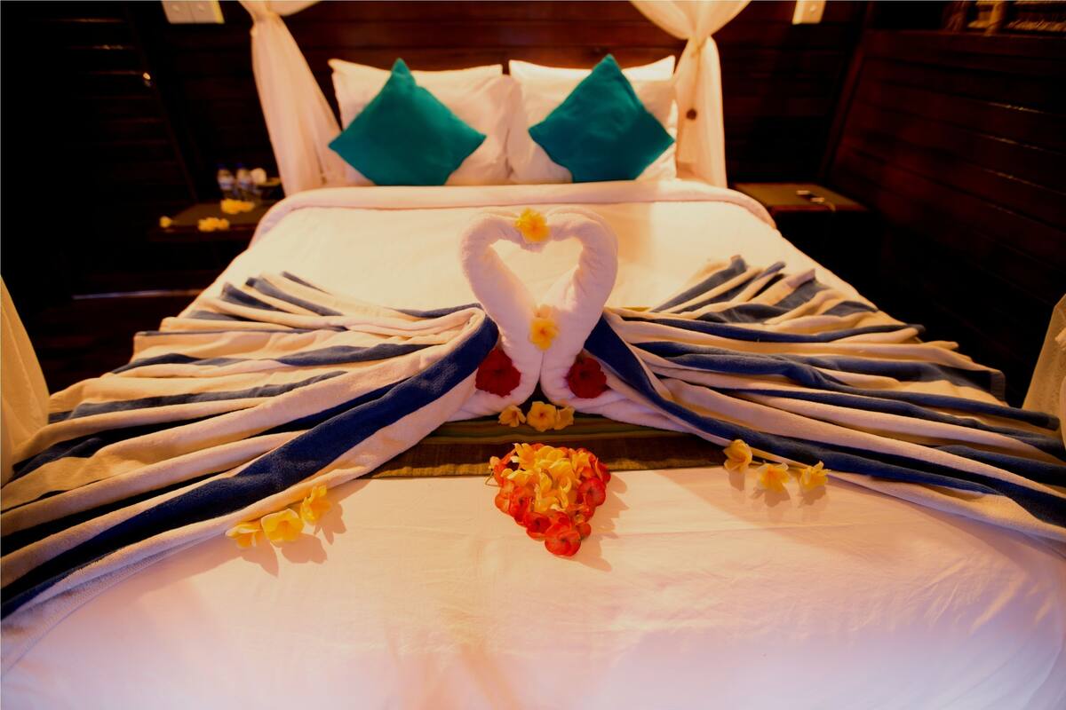 A neatly made bed with towels arranged in a heart shape and a flower centerpiece.
