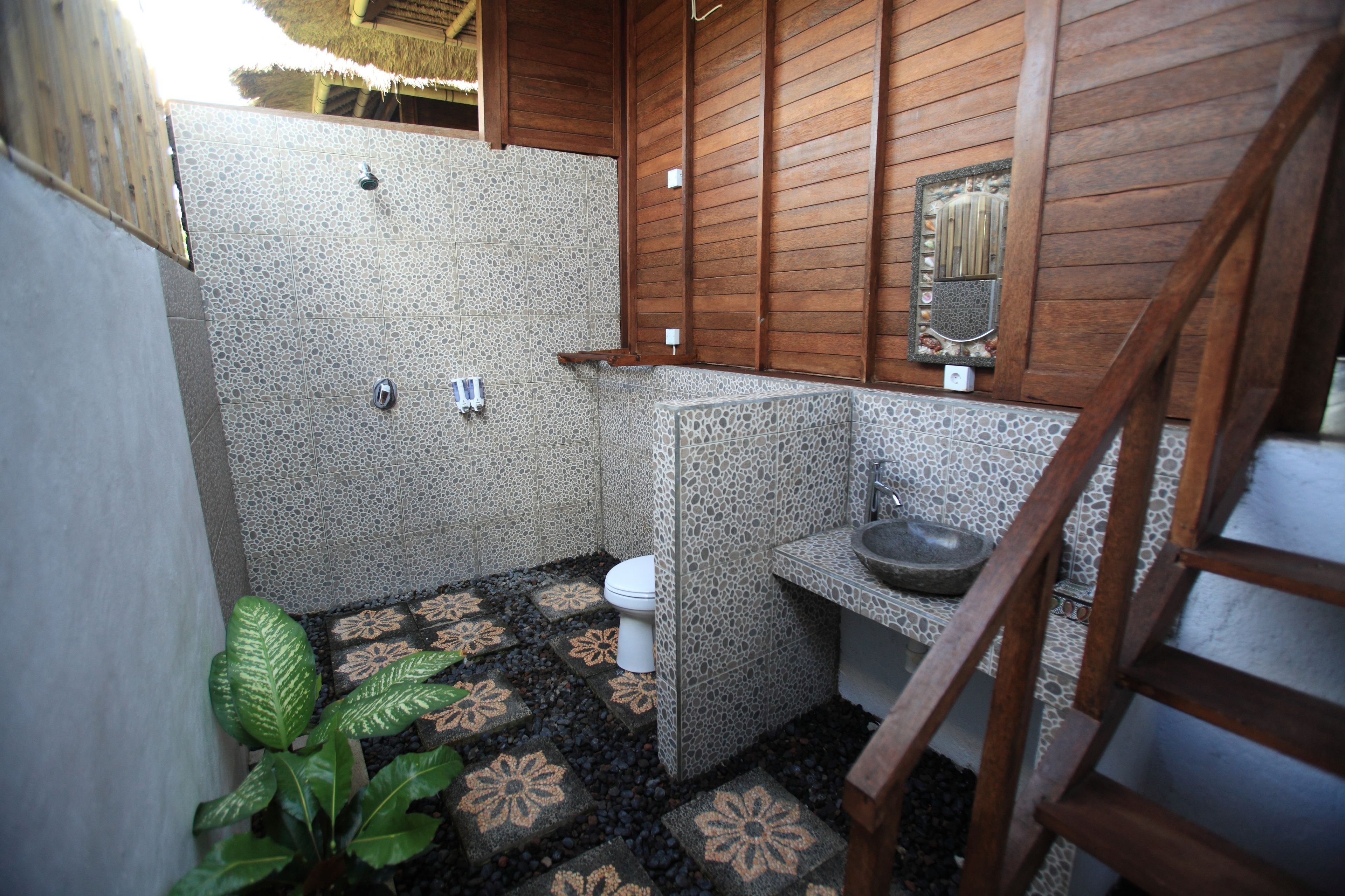A compact bathroom with a shower, toilet, and sink, featuring a mosaic floor and wooden paneling.