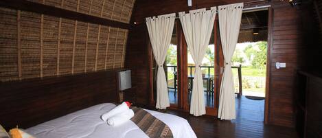 A wooden room with a bed, curtains, and a view of the outdoors.