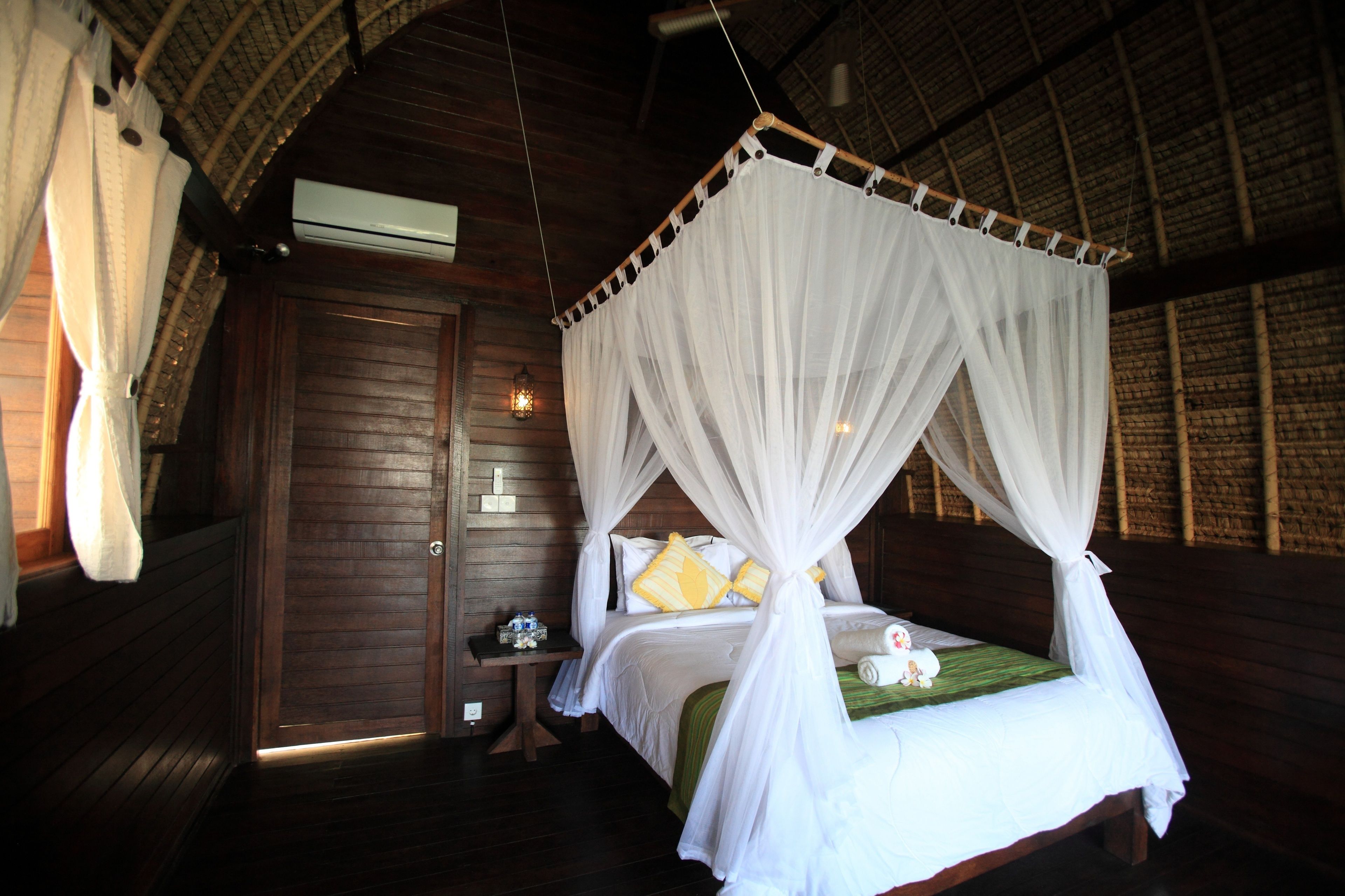 A four-poster bed with white canopy, wooden walls, and a small bedside table with a lamp.