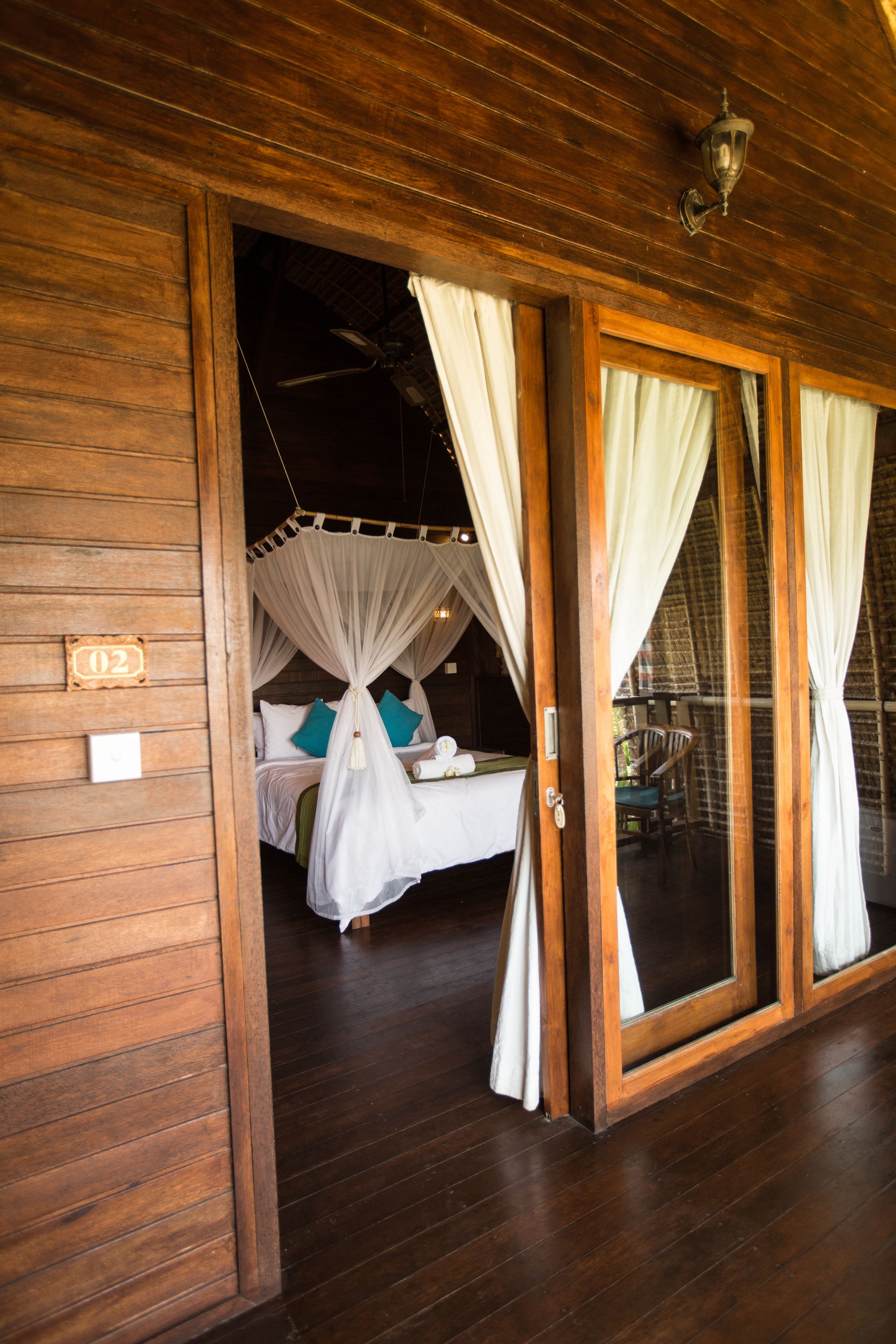 A wooden room with a bed, white curtains, and a number "02" sign.