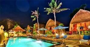 A pool area with lounge chairs and umbrellas, surrounded by thatched-roof huts and palm trees. - Sunset Coin Lembongan Cottage and Spa (Lembongan Island)