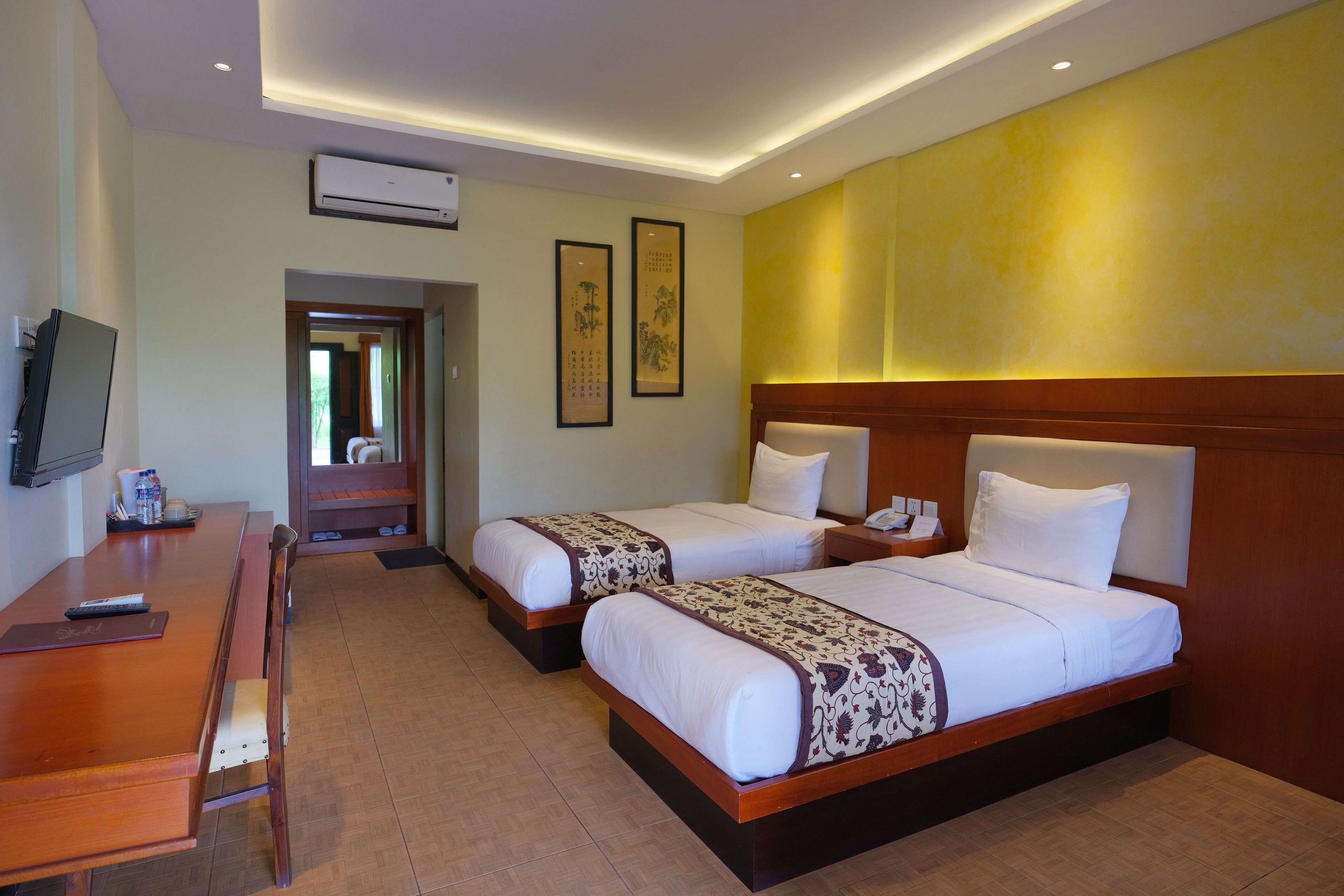 A hotel room with two beds, a wooden desk, a television, and framed artwork on the wall.