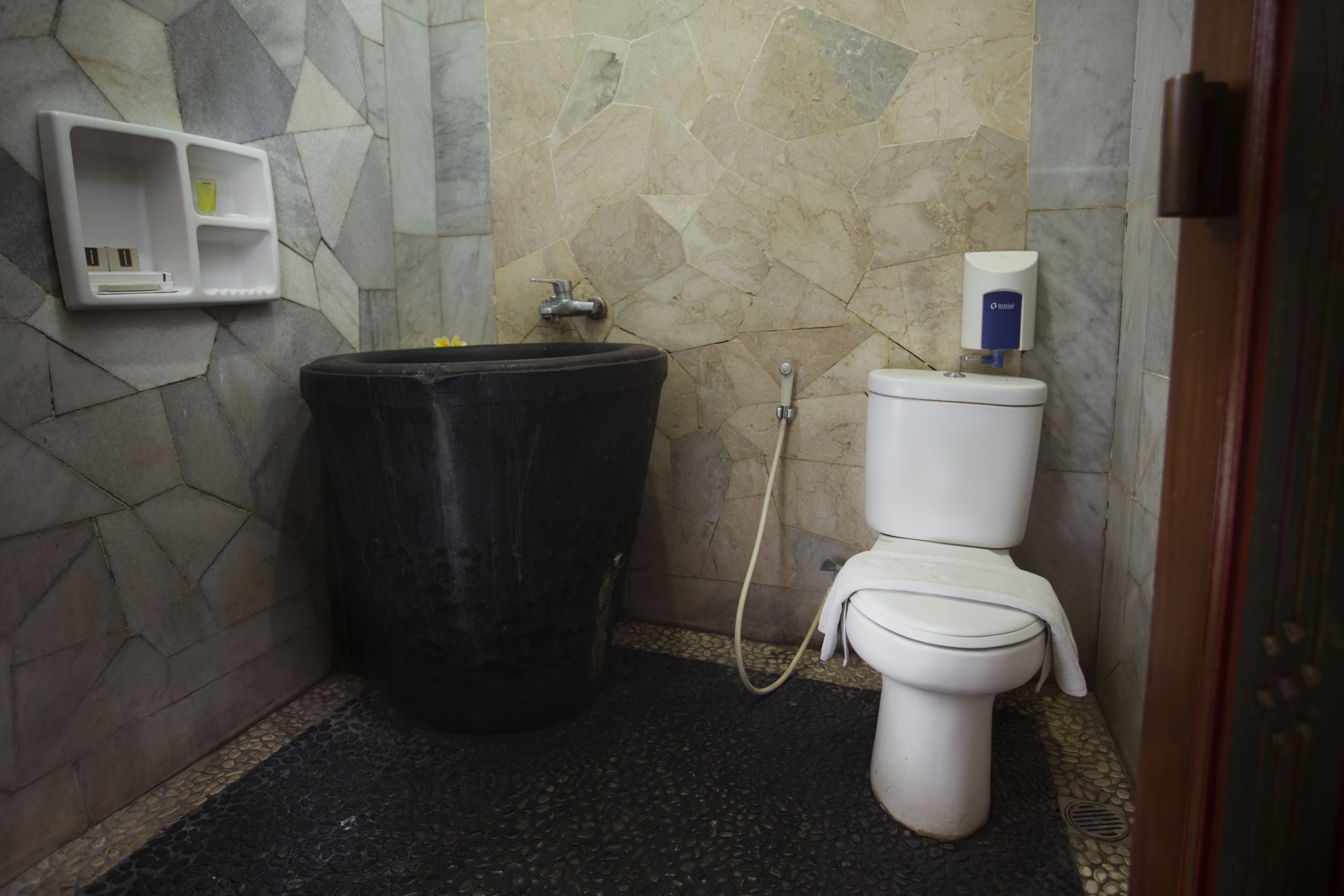 Un baño con un cubo de basura negro, un inodoro y un dispensador de jabón en la pared.