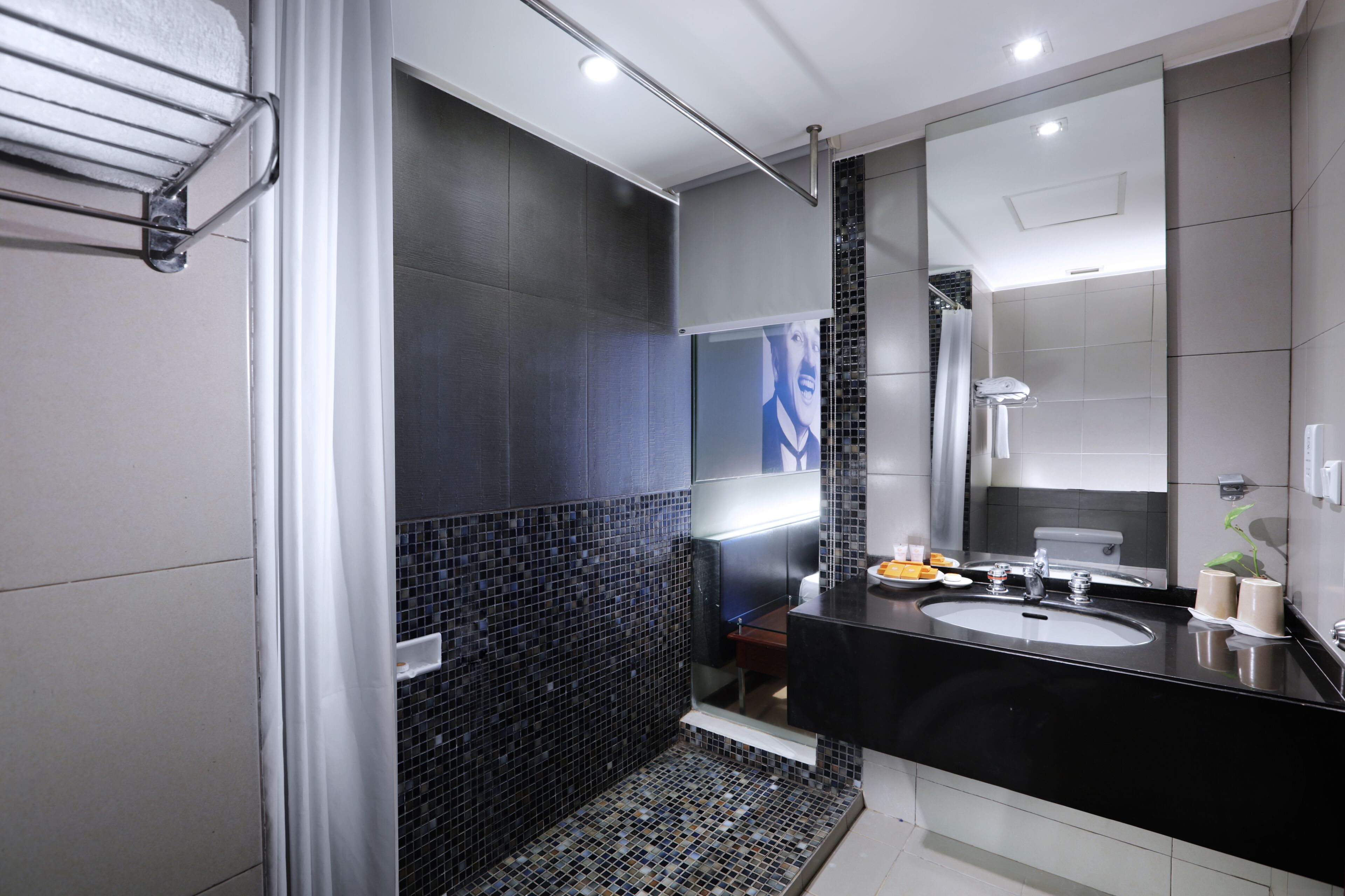 Un baño moderno con un lavamanos negro, un espejo grande y una zona de ducha con azulejos.