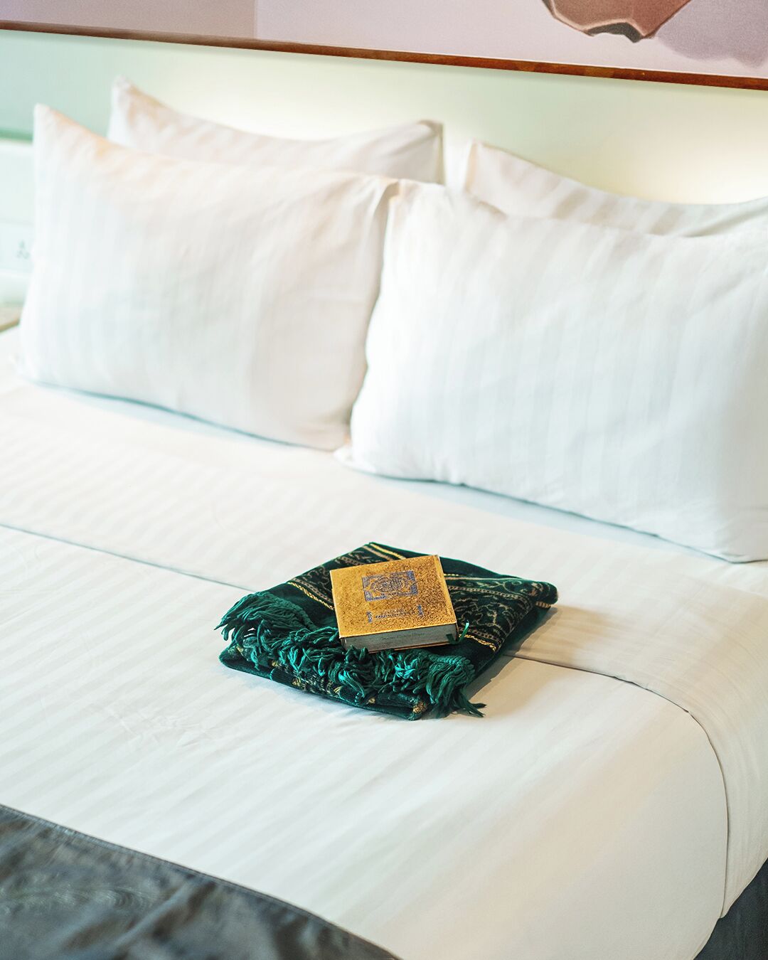 A bed with white linens, a green throw blanket, and a small book.
