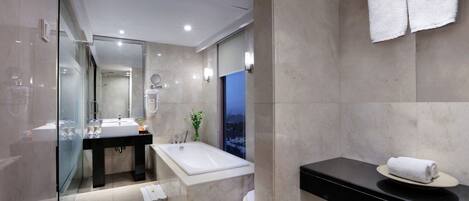 A modern bathroom with a glass shower enclosure, a large bathtub, a black countertop, and a view of the cityscape through the glass.