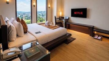 A modern hotel room with a large bed, a desk with a telephone, a laptop, and a television displaying 'NETFLIX'.