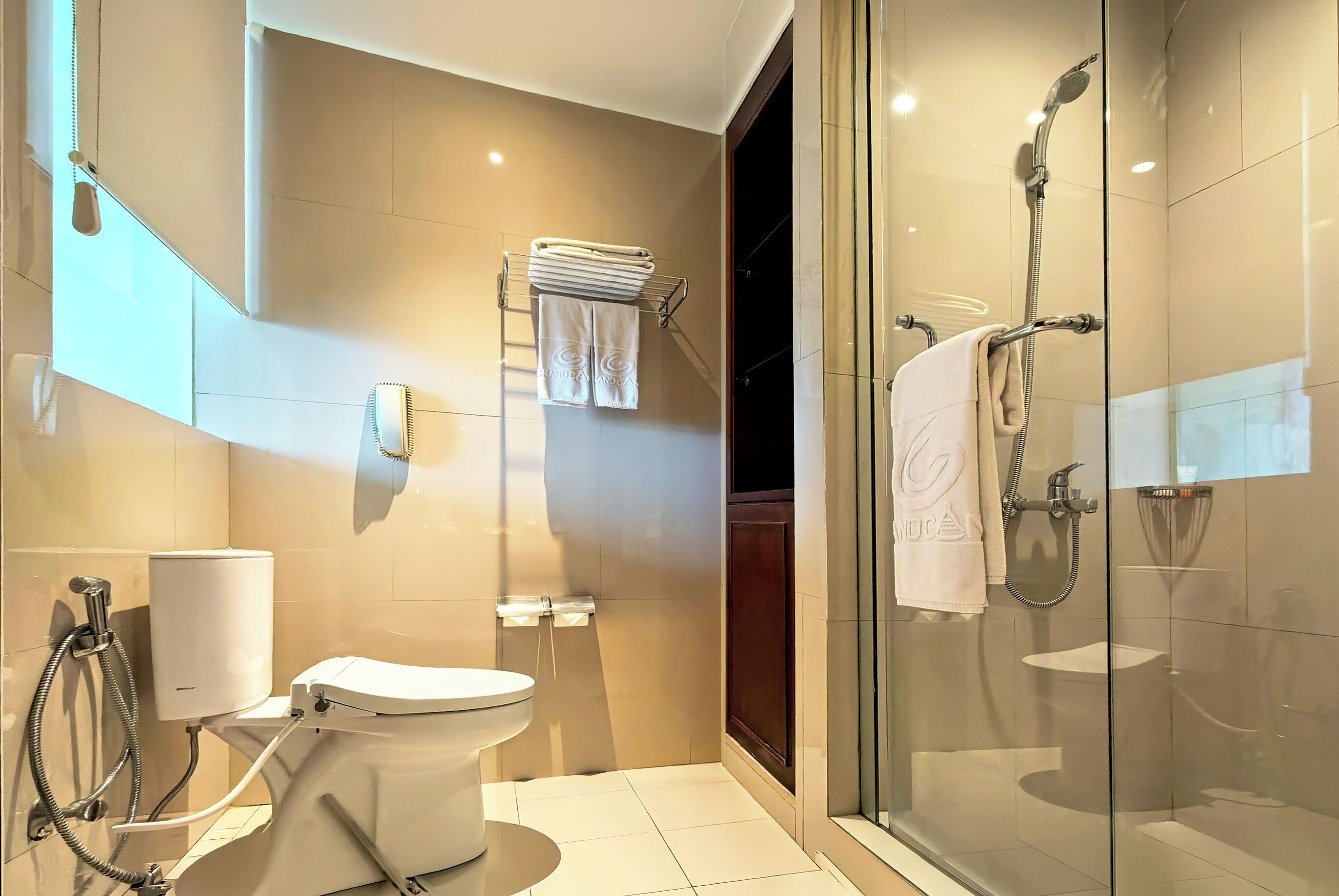 Un baño moderno con inodoro, bidé, cabina de ducha de vidrio y un perchero para toallas.