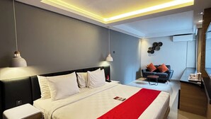 A modern hotel room with a large bed, bedside tables, a desk, and a seating area with a sofa and chairs. - @HOM Simpang Lima Semarang (Semarang)