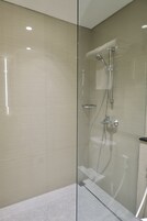 A modern bathroom with a glass shower enclosure, a handheld showerhead, and a wall-mounted faucet.