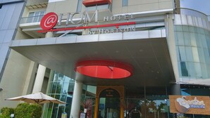 A hotel with a prominent red and white sign, a modern glass facade, and a large entrance canopy. - @HOM Simpang Lima Semarang (Semarang)