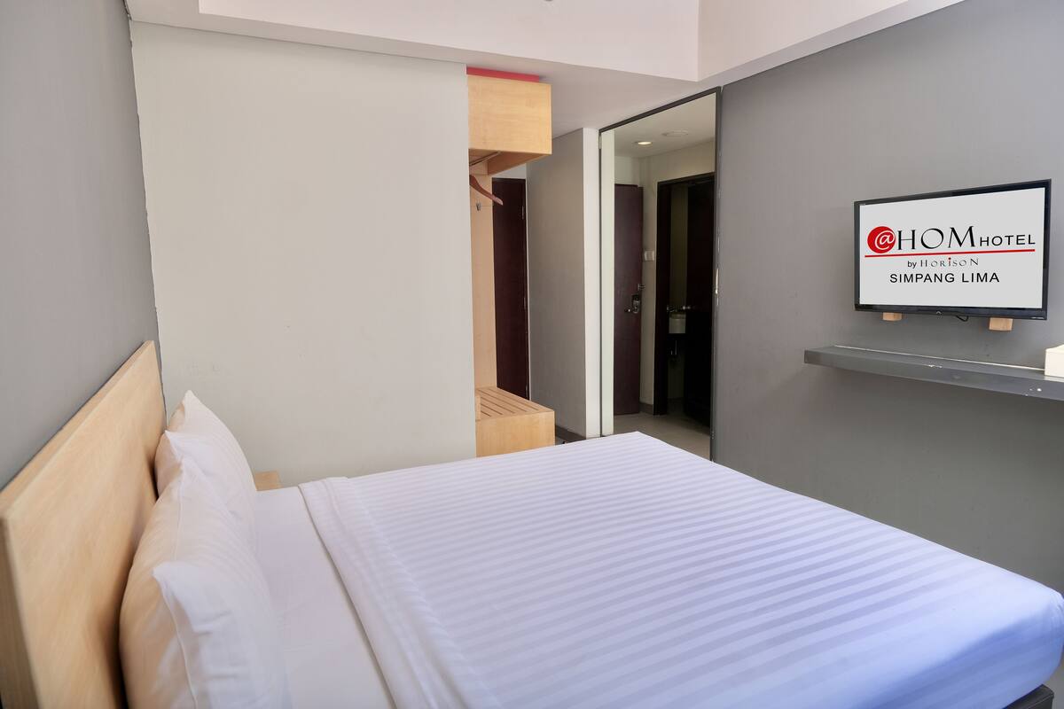 Quarto de hotel com cama, espelho e um aviso na parede.