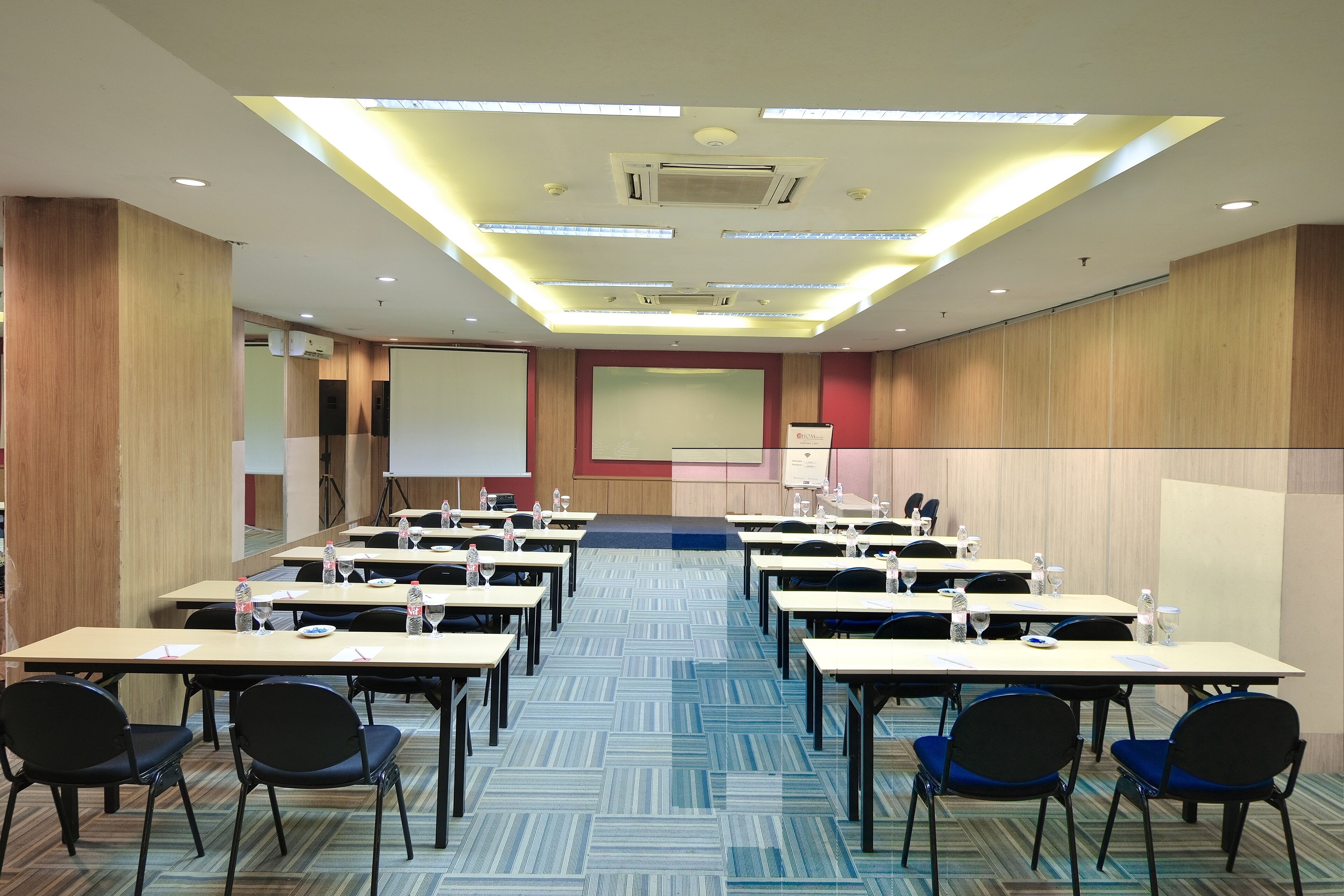 A conference room with multiple tables and chairs, equipped with water bottles and glasses, and a presentation screen at the front.