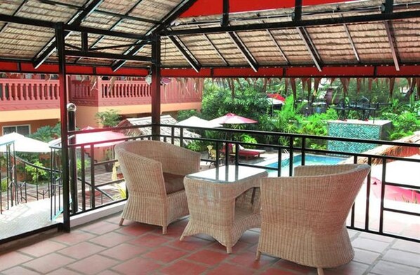 A covered outdoor seating area with wicker furniture and a view of a swimming pool and greenery.