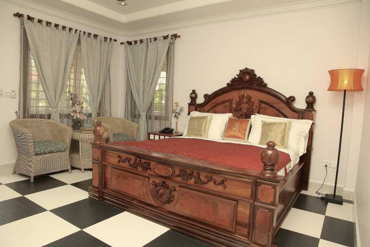 Un dormitorio con una cama de madera grande, una silla, una mesita de noche y una lámpara de pie.