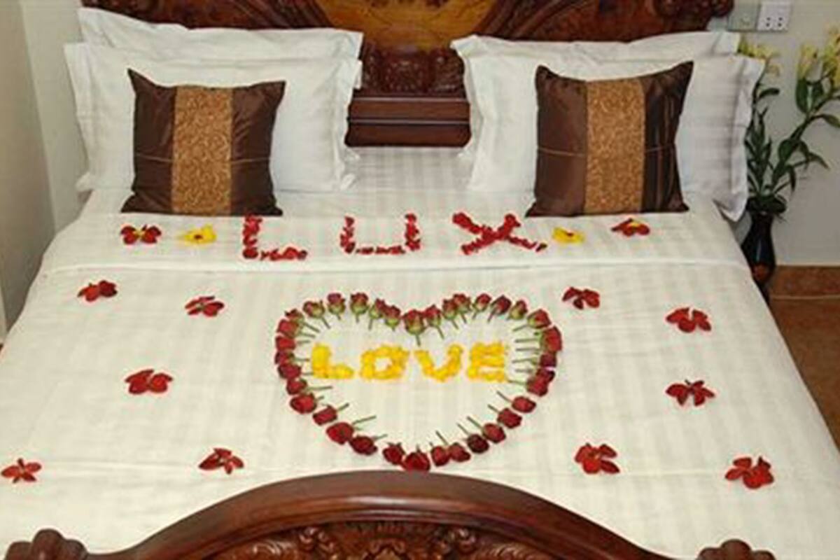 Una cama con un arreglo de flores en forma de corazón que deletrea 'LOVE' y pétalos dispersos sobre un edredón blanco.