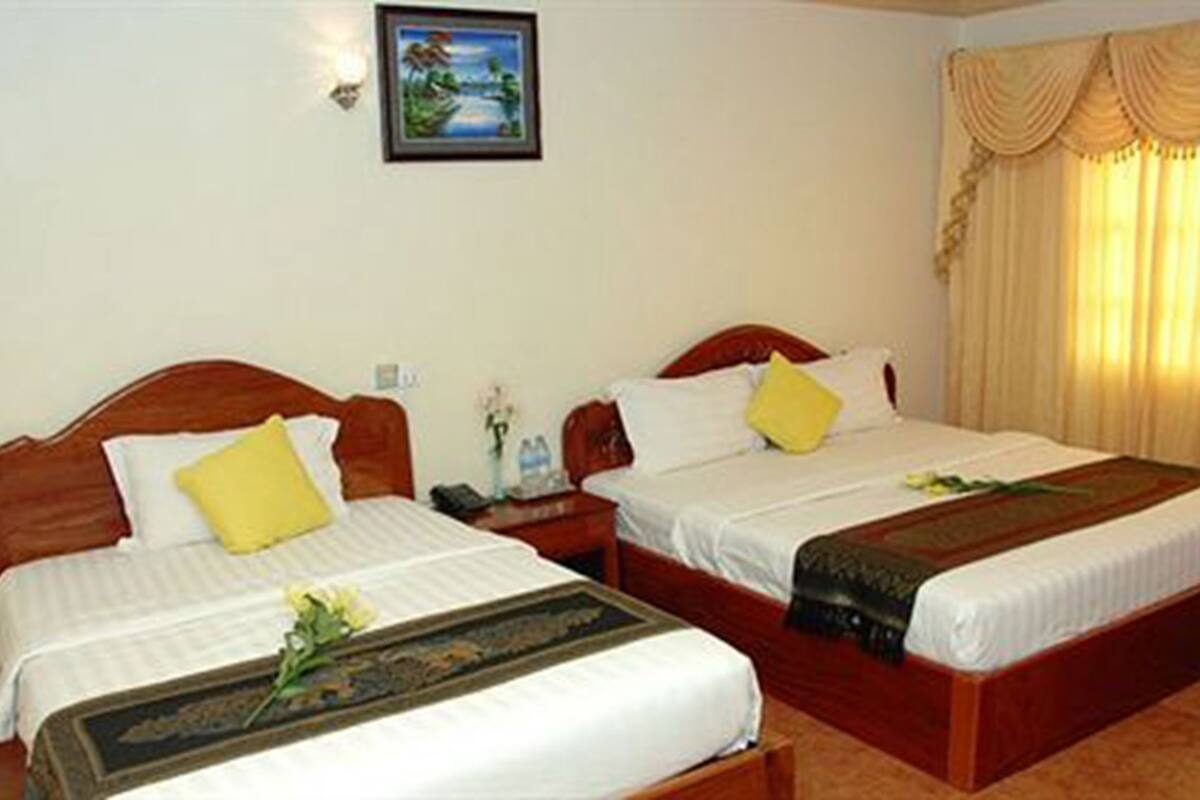 Habitación de hotel con dos camas individuales, una mesita de noche, un cuadro enmarcado en la pared y una ventana con cortinas.