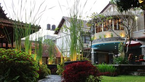 A courtyard with a stone pathway, red foliage, and a pool area with chairs. - Hotel Sriti (Magelang)