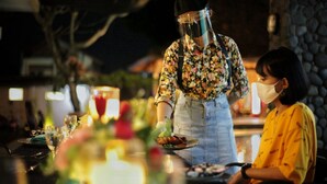 A person serving food at an outdoor dining area with a stone wall and greenery in the background. - Hotel Sriti (Magelang)