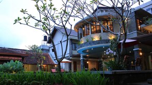 A modern hotel with a curved balcony, outdoor seating, and a well-maintained garden. - Hotel Sriti (Magelang)