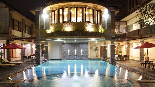 A swimming pool with a fountain, surrounded by stone pillars and outdoor seating. - Hotel Sriti (Magelang)