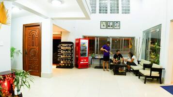 A lobby with a wooden door, a Coca-Cola refrigerator, seating area, and a plant.