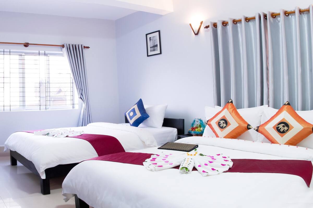 Une chambre d’hôtel avec deux lits, une fenêtre avec des rideaux, un tableau au mur et une table de chevet avec une lampe.