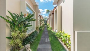 A narrow pathway flanked by buildings with large windows and potted plants. - Svarna Suite Seminyak (Legian)