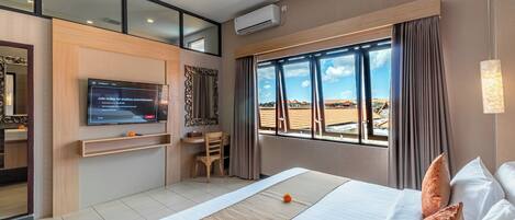 A hotel room with a bed, a TV, a window with curtains, and a view of buildings.