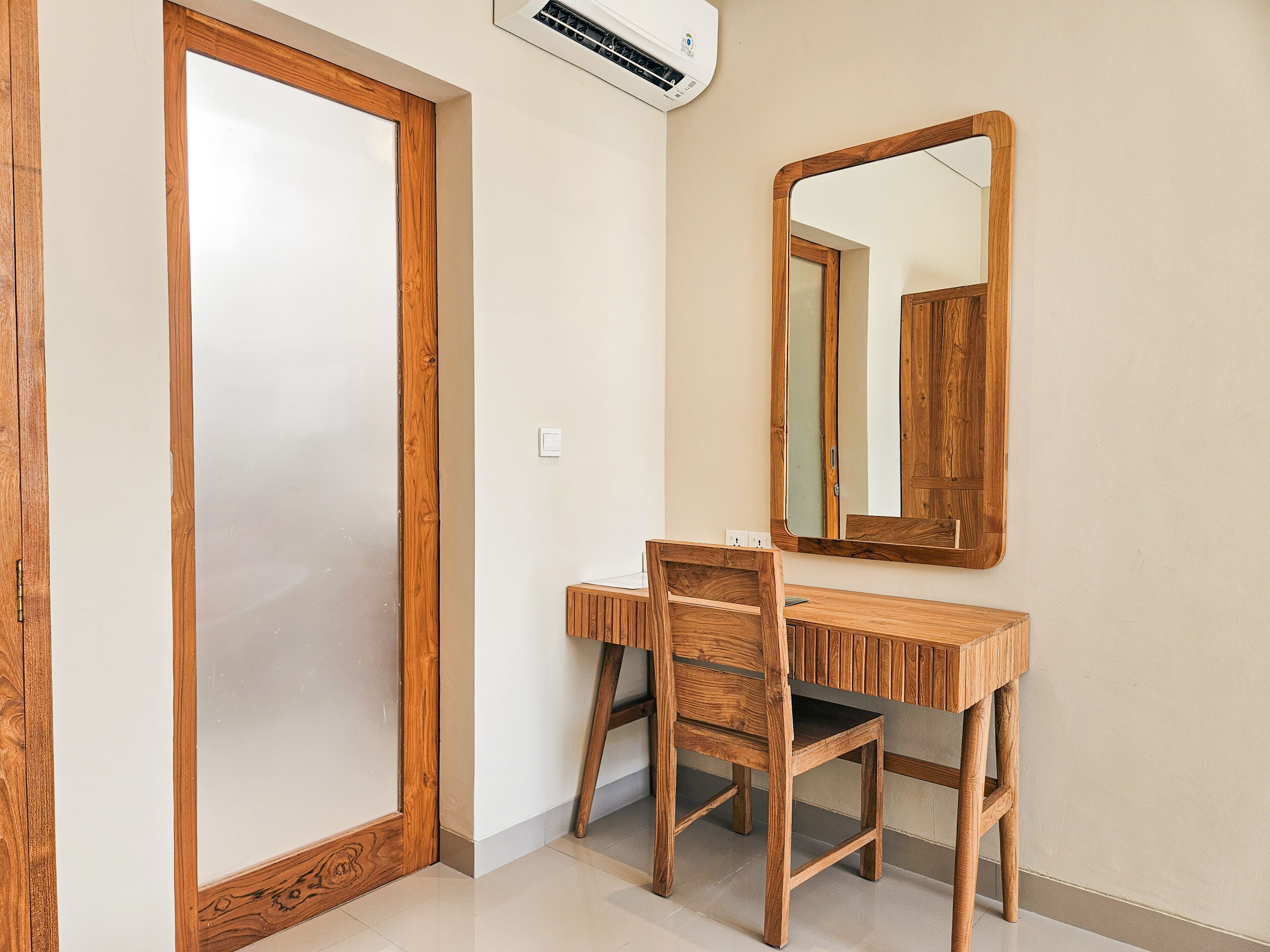 Une pièce avec un bureau et une chaise en bois, un grand miroir et une porte dotée d’un panneau en verre dépoli.