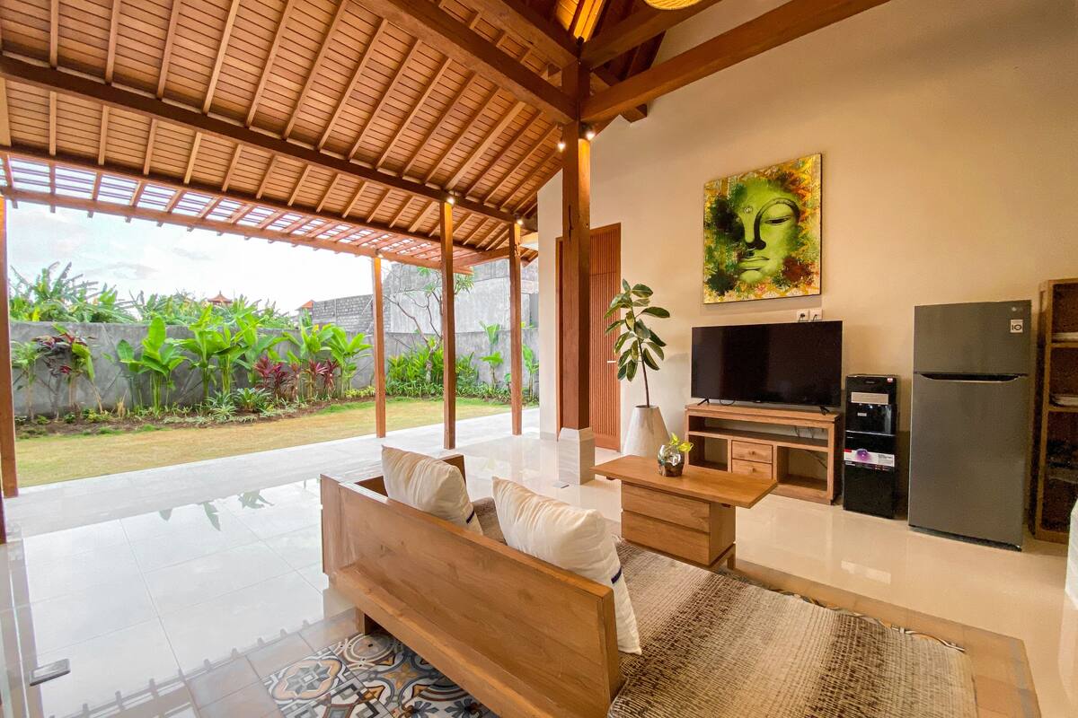 A modern living room with a wooden sofa, a flat-screen TV, a refrigerator, and a dining area.