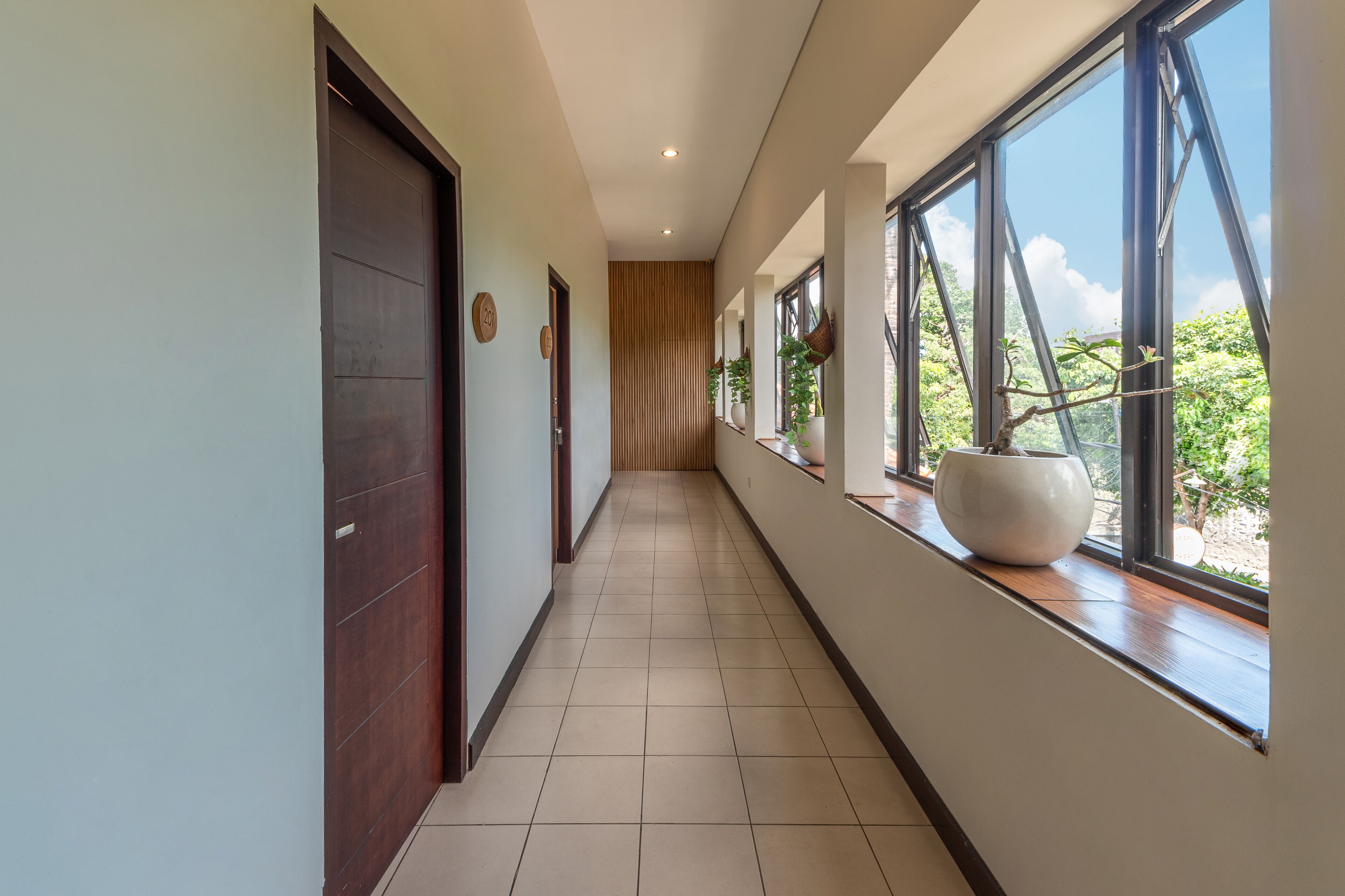 A modern hallway with large windows, a wooden door, and a tiled floor.