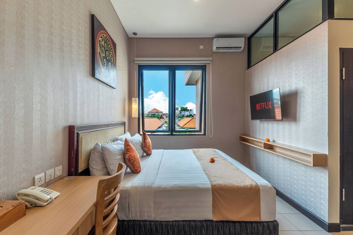 A hotel room with a bed, bedside table, chair, and a TV mounted on the wall.