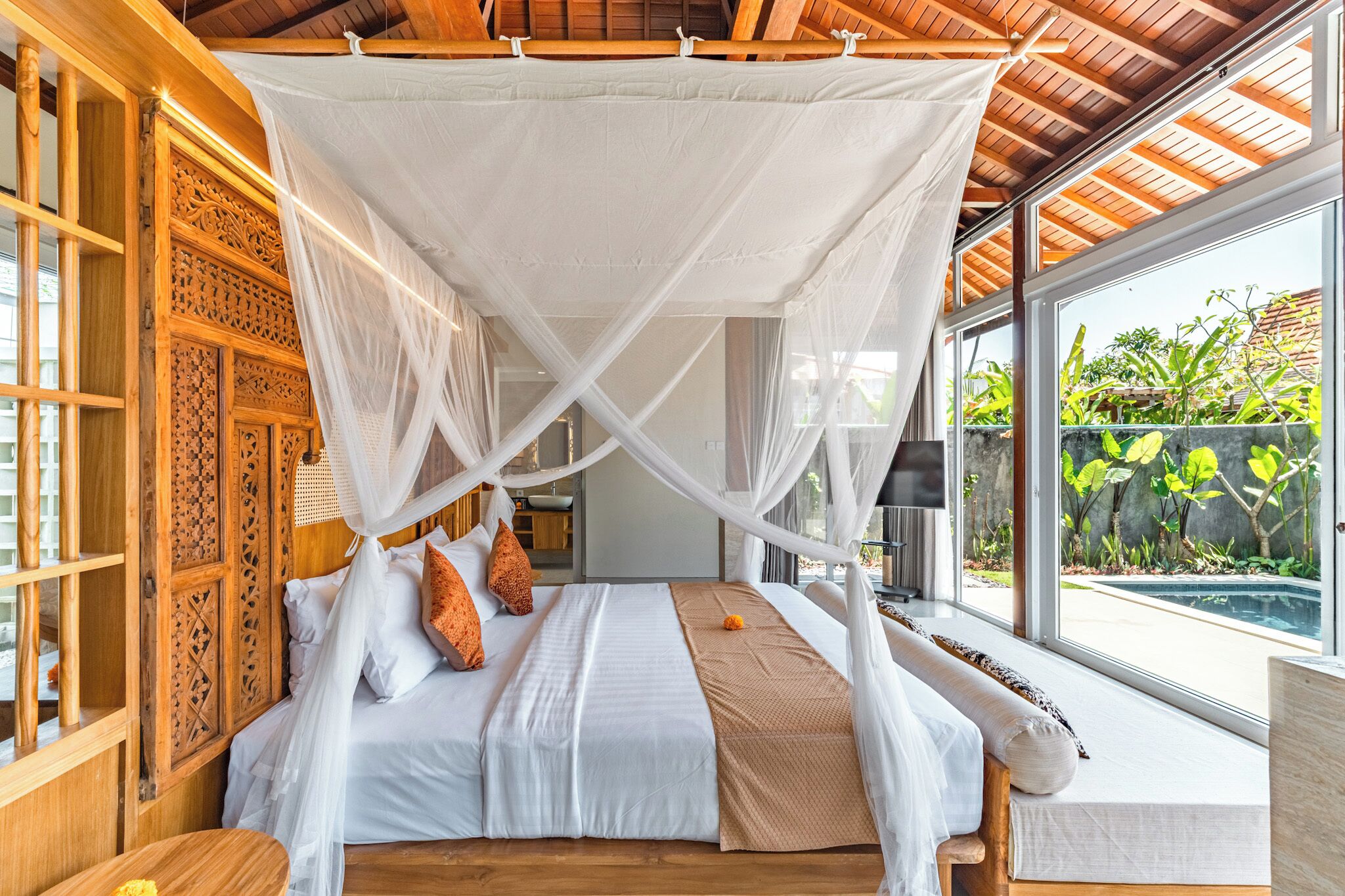 Ein Schlafzimmer mit Baldachinbett, Holzmöbeln und Blick auf einen Swimmingpool.