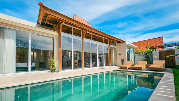 A modern house with a swimming pool, large sliding glass doors, and outdoor seating. - Svarna Suite Seminyak (Legian)