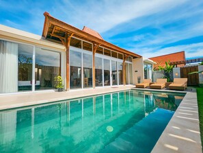 A modern house with a swimming pool, large sliding glass doors, and outdoor seating. - Svarna Suite Seminyak (Legian)