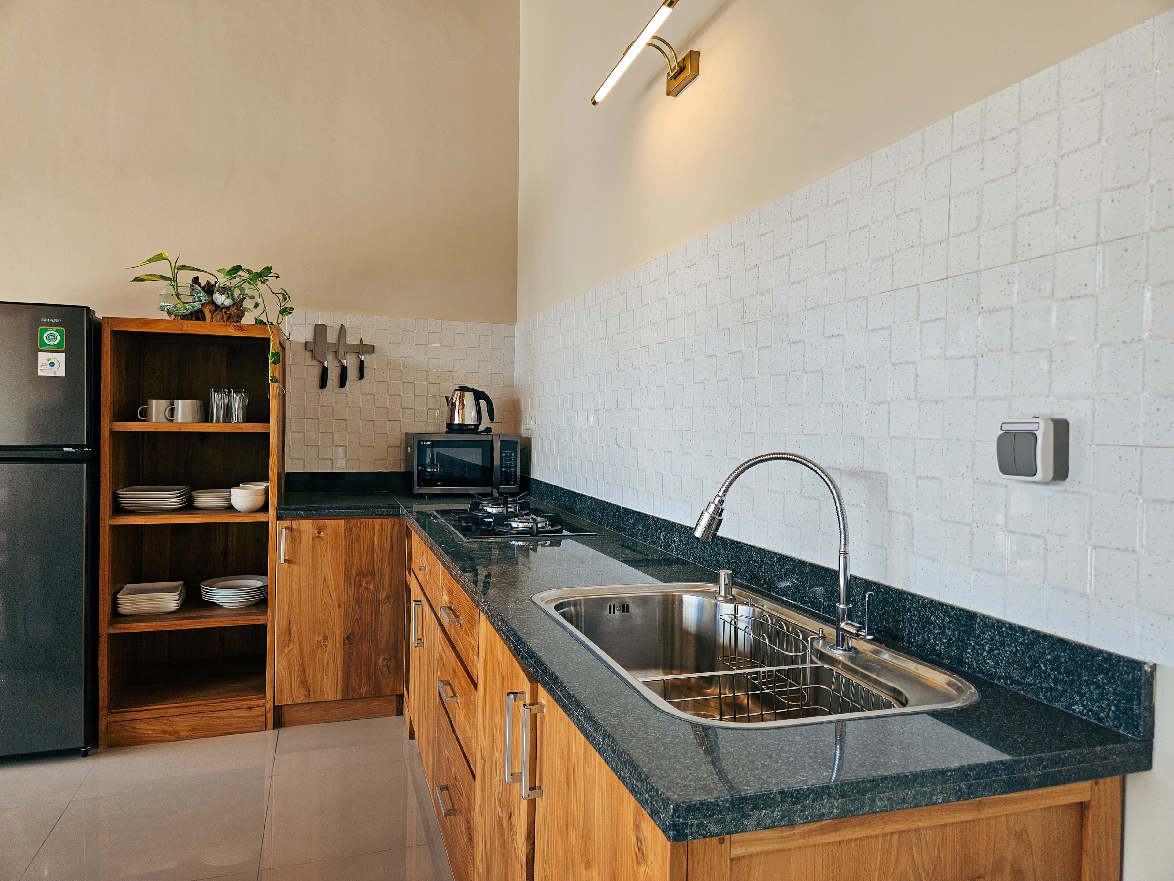 A modern kitchen with a granite countertop, stainless steel sink, wooden cabinets, a microwave, and a kettle.