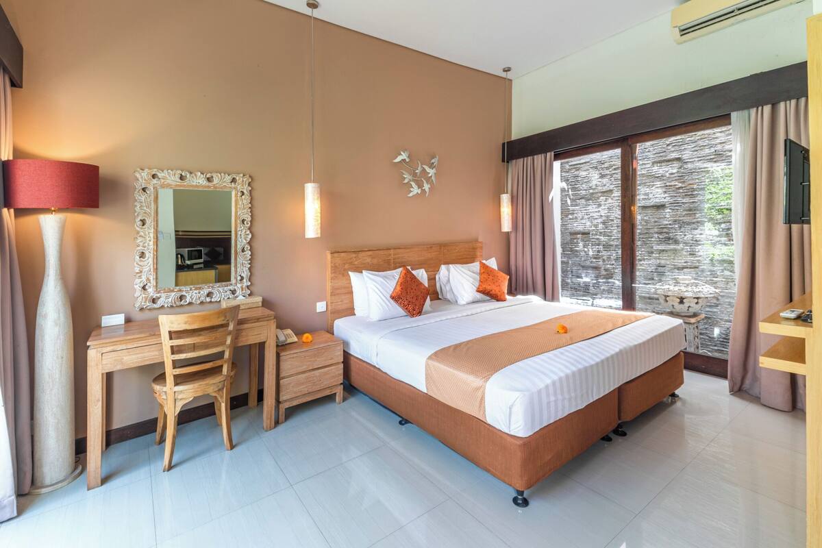 A hotel room with a large bed, a desk with a chair, a mirror, and a window with curtains.