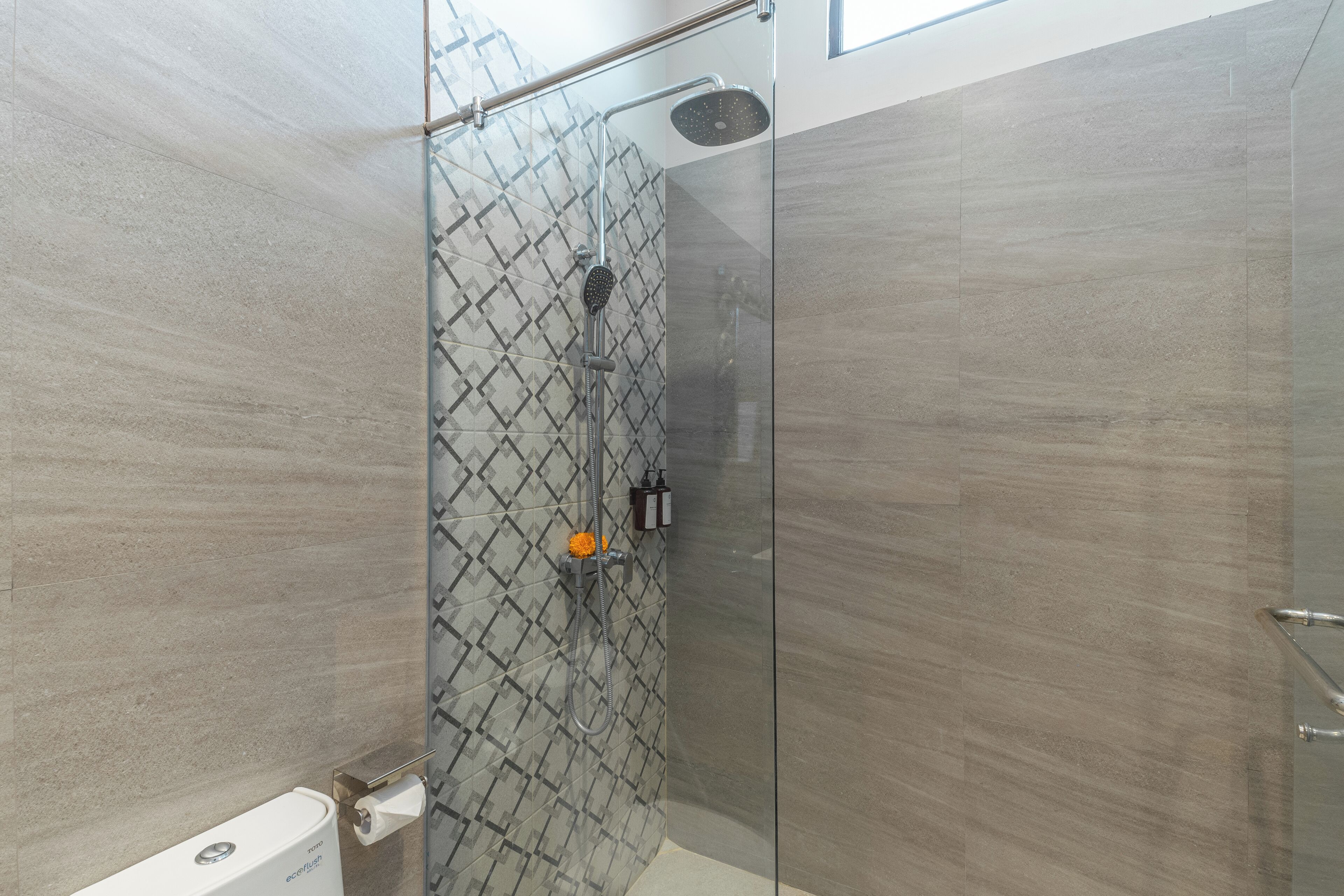 A modern shower with a glass door, a handheld showerhead, and a wall-mounted control panel.