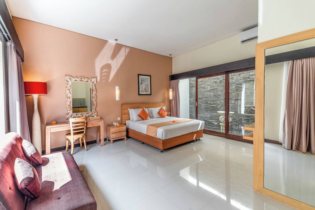 A modern hotel room with a large bed, a desk, a chair, a sofa, and a large mirror.