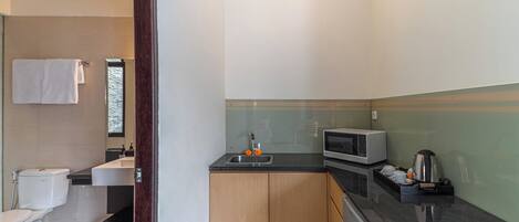 A compact kitchen with a sink, microwave, and kettle, adjacent to a toilet and a small window.